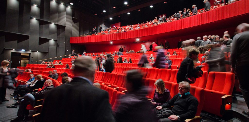 Illustrasjonsfoto av operasalen, med publikum som er på veg til seta sine. Personane er ganske uklare og uidentifiserbare og i fart.
